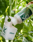 une image d'une petite boîte blanche étiquetée "dibox", suspendue à une plante sur un fond flou