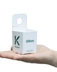 Une petite boîte de distribution dibox en carton blanc avec un "K" vert et la marque "Dibox", tenue dans la main d'une personne.
