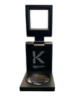 A black metal magnifying lens with a scale, displayed alongside its black protective case, featuring the brand name 'Koppert' on the lens.