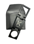 A black metal magnifying lens with a scale, displayed alongside its black protective case, featuring the brand name 'Koppert' on the lens.